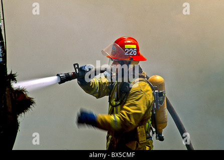 Wearing safety equipment and an air mask a firemen sprays water on a home blaze in Laguna Niguel, CA. Stock Photo