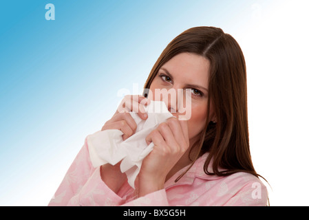 brunette woman blowing her nose wearing pyjamas Stock Photo