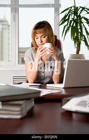Photo of attractive woman sitting at workplace in the office and drinking tea Stock Photo