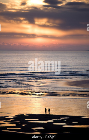 Man and woman in silhouette looking out over North Sea at sunsrise from Alnmouth Beach, near Alnwick, orthumberland, England, UK Stock Photo