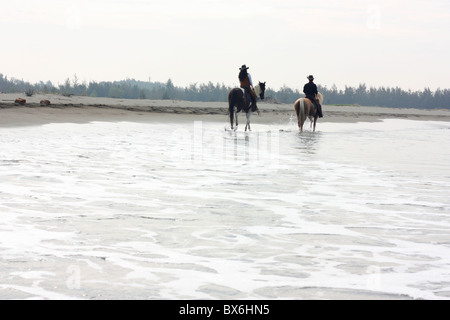 Two people ride horses together at the beach. Tainan, Taiwan Stock Photo