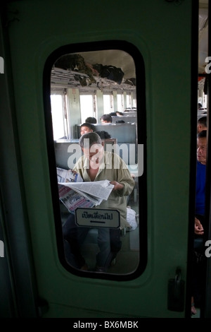 A man is reading a newspaper on a Bangkok bound passenger train in Ubon Ratchathani Province, Thailand. Stock Photo