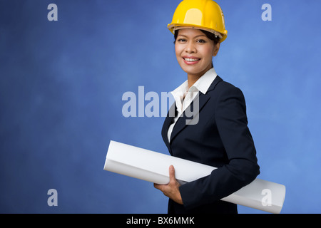 Portrait of pretty female with blueprints in hands and helmet on head smiling Stock Photo