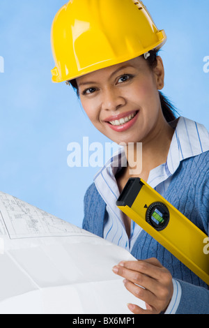 Portrait of pretty female with blueprints in hands and helmet on head smiling Stock Photo