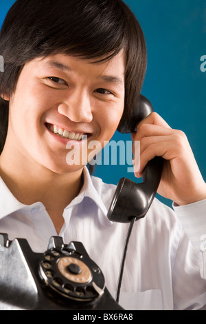 Image of happy Asian man holding telephone receiver and smiling Stock Photo