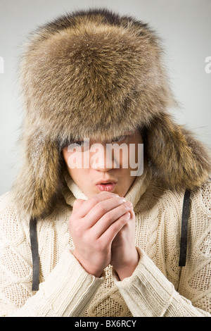 Portrait of cold man in fur hat and knitted sweater warming up his hands Stock Photo