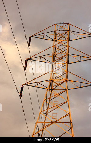 Transmission tower and power lines with bright sunset light shining on them, Stanislaus County, California, U.S.A. Stock Photo