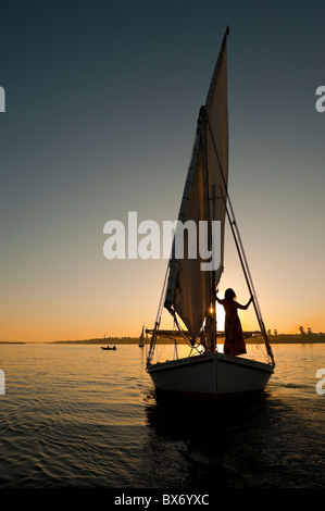 A stunning and beautiful image of a traditional Egyptian sail boat called a felucca on the Nile at sunset with girl on board Stock Photo
