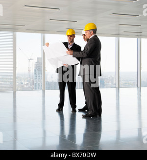 Three executives in hardhats looking at plans in empty office space Stock Photo