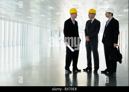 Three executives in hardhats in empty office space Stock Photo
