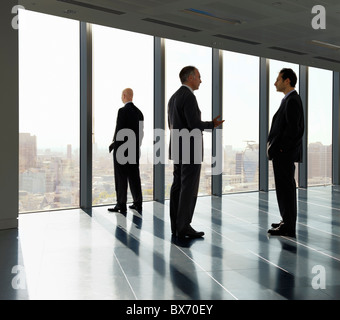 Three executives standing by window in empty office space with view over city landscape Stock Photo