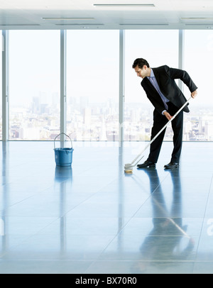 Businessman cleaning the floor in empty office, city landscape in background Stock Photo