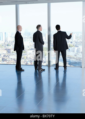 Three executives looking at city landscape in empty office space Stock Photo