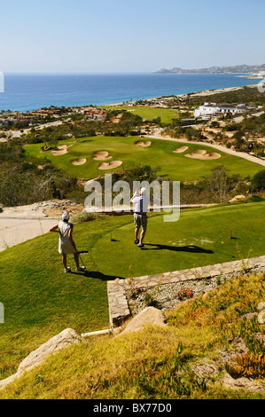 Couple playing golf along Pacific Ocean at Puerto Los Cabo Golf Club in San Jose del Cabo in Baja, Mexico Stock Photo