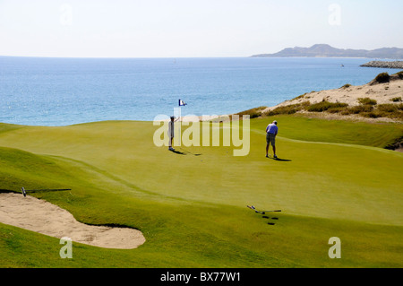 Couple playing golf along Pacific Ocean at Puerto Los Cabo Golf Club in San Jose del Cabo in Baja, Mexico Stock Photo