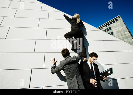 2 men helping woman over wall Stock Photo