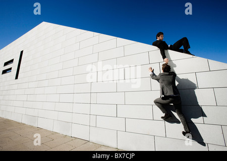 Man helping other man over wall Stock Photo