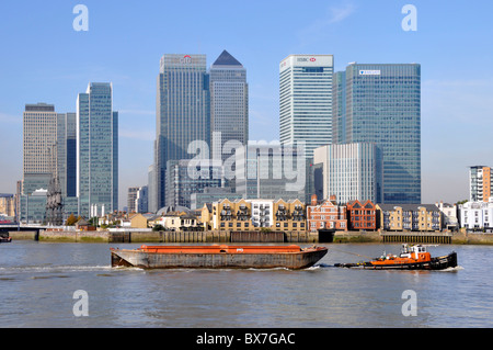 Tugboat large empty barge on River Thames passing some of major banking business headquarters skyscraper buildings at Canary Wharf London Docklands UK Stock Photo