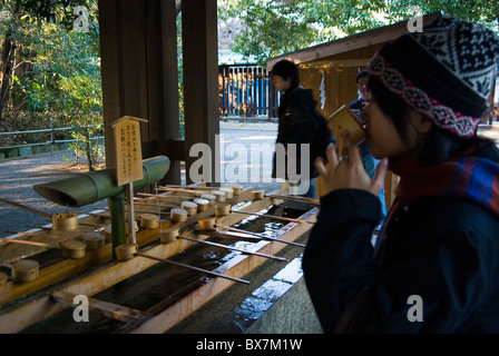 japanese girl drinkin from ritual fountain at meiji jingu shrine during shogatsu new year's celebrations, tokyo, japan Stock Photo