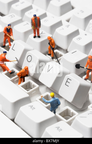 Stock photo of worker figurines posed around the word love spelled out with compute keys, on a keyboard. Stock Photo