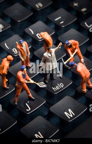 Worker figurines posed to look as though they are working on a computer keyboard. Stock Photo