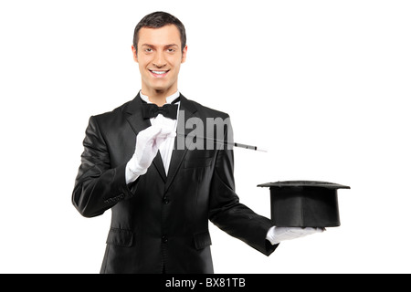A magician in a black suit holding an empty top hat and magic wand Stock Photo