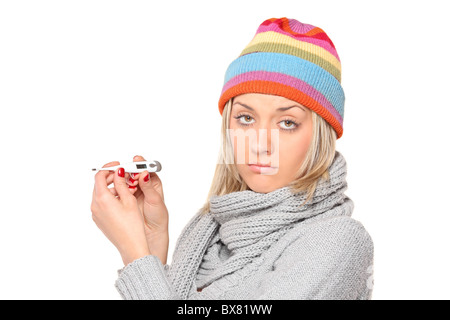 Ill woman wearing a cap and scarf with thermometer in her hands Stock Photo