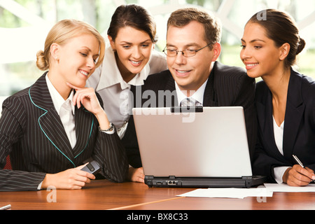 Portrait of four businesspeople sitting at the table in front of opened laptop and seriously gazing at the screen Stock Photo