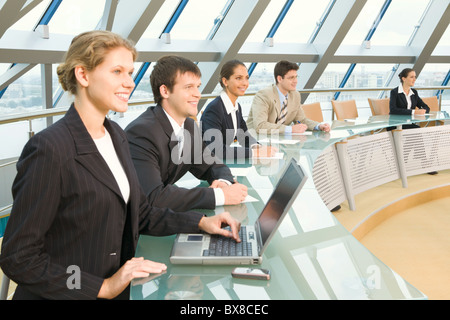Businesspeople sitting at the round table in large light conference hall with glassy walls discussing important questions Stock Photo