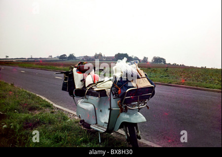 Original 60'simage of a scooter/moped parked up by the side of the road in the country. The scooter is laden down with luggage. Stock Photo