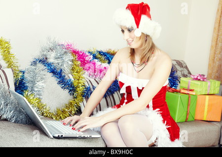 Smiling lady sitting indoors in Santa Claus costume making online Christmas greeting Stock Photo