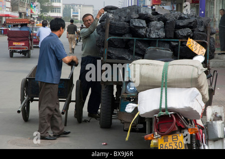 Man delivering coal from a heavily loaded motor tricycle in Datong, Shanxi, China. Stock Photo