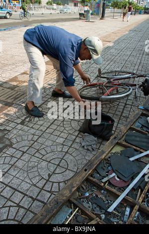 Man repairing the tube tyre of a bicycle on a sidewalk in Datong, Shanxi, China. Stock Photo