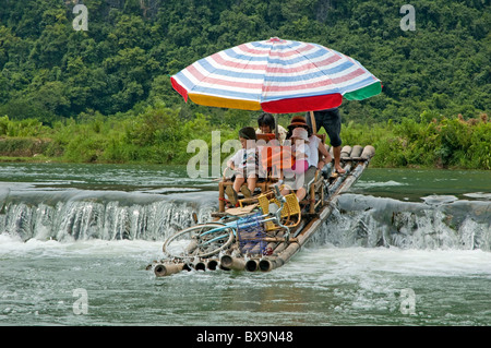 Family of European tourists on a bamboo raft passing over a dike on the Yulong River, Yangshuo, Guangxi, China. Stock Photo