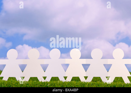 Concept image of paper women holding hands in a field with sky background Stock Photo
