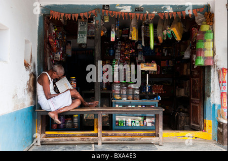 Indian man sitting reading outside a rural South Indian village shop Stock Photo