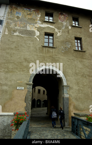 Two young women walking through arched building passageway from pedestrian bridge over Adda River in village of Tirano Italy Stock Photo