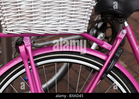 Close-up of the saddle and rear wheel of a pink bicycle with white wicker basket. Stock Photo