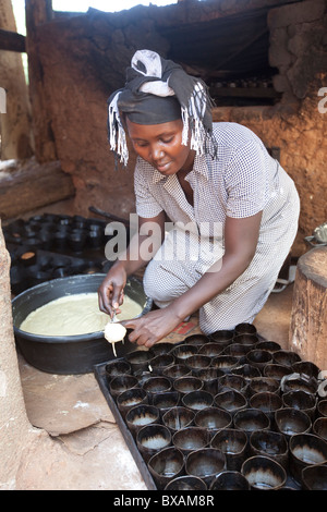 A baker (Rehama Mbabazi) pours batter into a cakepan in Mutukula Village, Iganga district, Eastern Uganda, East Africa. Stock Photo