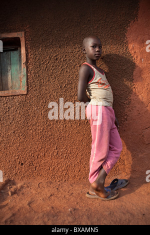 A boy stands alone outside a mud house in Jinja, Uganda, East Africa Stock Photo