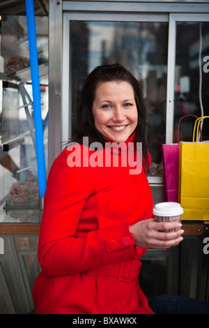 Portrait of young woman holding takeaway coffee, with shopping bags in background Stock Photo