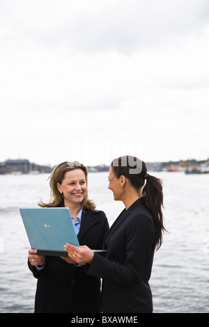 Pair of businesswomen working on laptop by canal Stock Photo