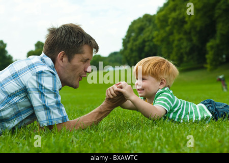 Father and son lying on lawn in park and playing Stock Photo