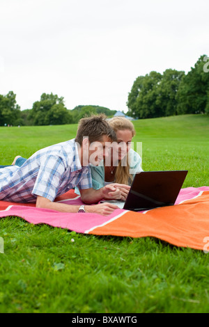 Mid adult couple lying on blanket and using laptop Stock Photo