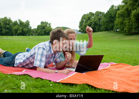 Happy couple lying in park and using laptop Stock Photo