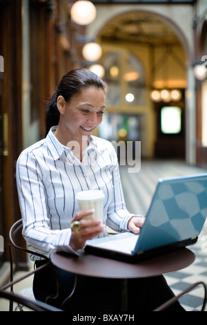 Mature businesswoman working on laptop, holding takeaway coffee Stock Photo