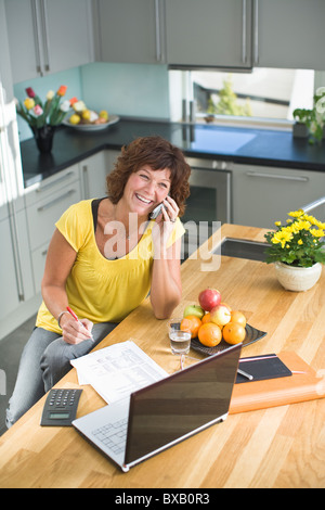 Woman sitting with bills and talking on mobile phone Stock Photo