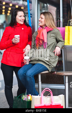 Pair of young women taking break from shopping, drinking takeaway coffee Stock Photo