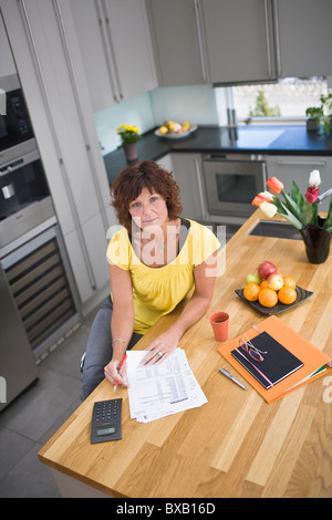 Woman sitting in kitchen with bills, portrait Stock Photo