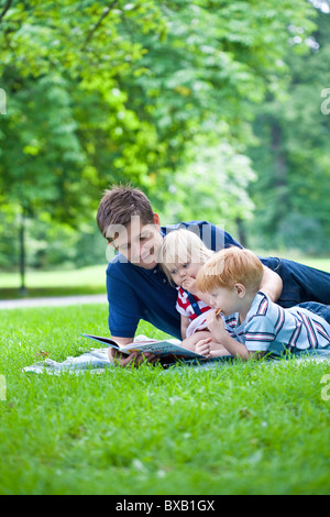 Father reading book to son and daughter in park Stock Photo